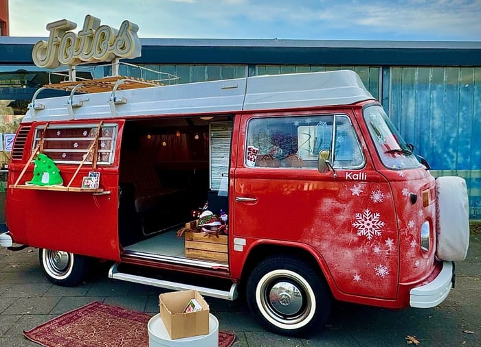 Roter VW-Bulli in voller Seitenansicht mit weißen Schneeflocken-Aufklebern und Leuchtschrift Fotos auf dem Dach.