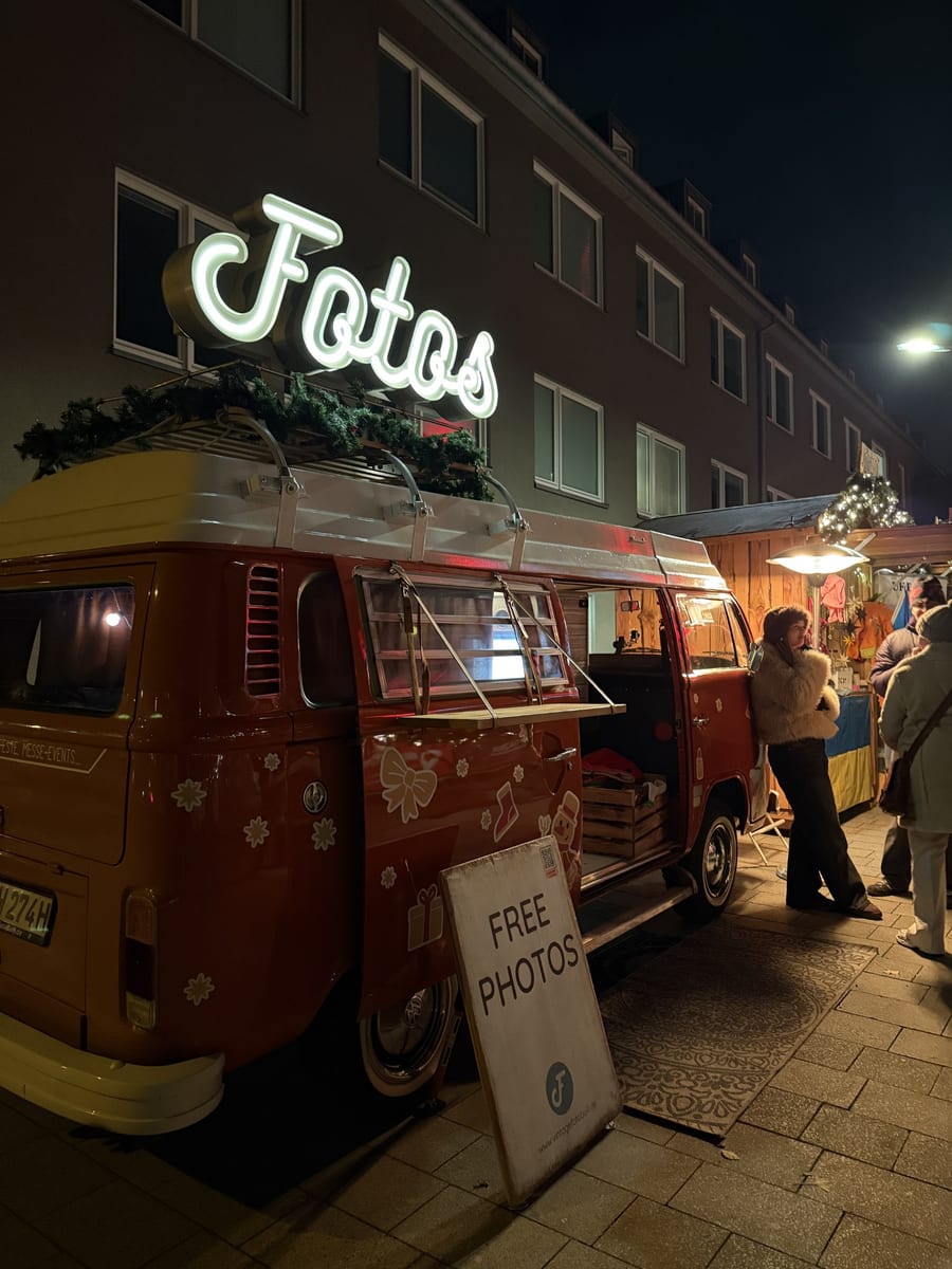 Der rote Foto Bulli bei Nacht auf dem Weihnachtsmarkt, eine Besucherin lehnt an der offenen Tür.